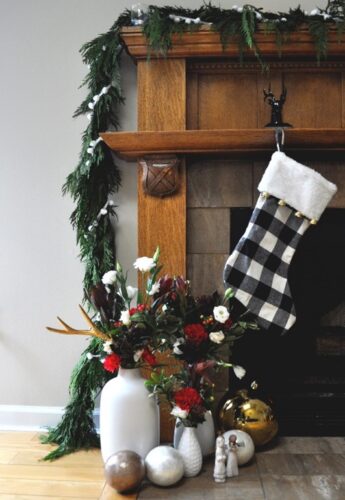 Black and white plaid stocking hanging over fireplace beside thrifted vases