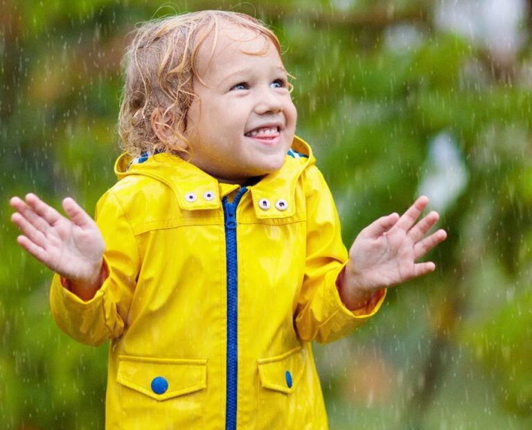 Toddler in yellow rubber raincoat standing in the rain
