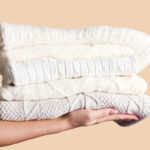 Person holding out a stacked pile of fall / winter sweaters in neutral colours to as a donation of gently used clothing goods