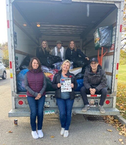 The Hanlon Team of 5 people sitting inside the back of a truck with bags of donations from their community donation drive