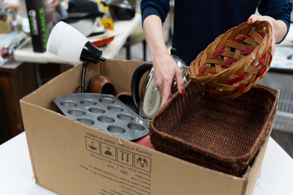 Box full of household donations like baskets and bakeware