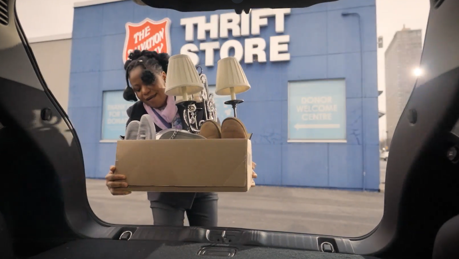 Woman takes box of household donations out of her vehicle trunk in Thrift Store parking lot