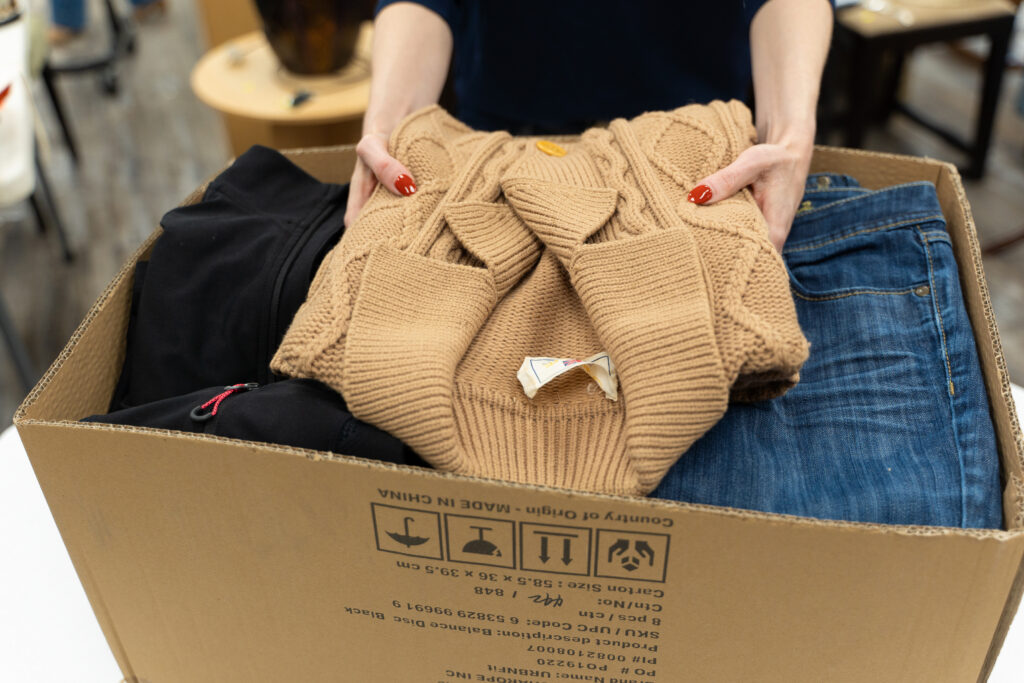 Box full of clothing to donate and women holding a beige sweater to add in the box