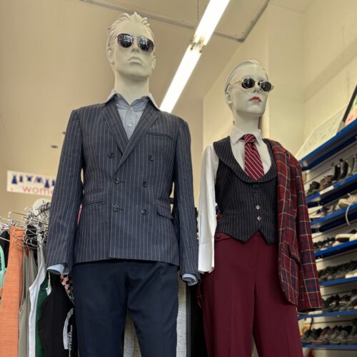 workwear outfits including blazer, dress shirt, and sunglasses on a male mannequin and a vest, tie, collar top, and sunglasses on a female mannequin featured inside Thrift Store