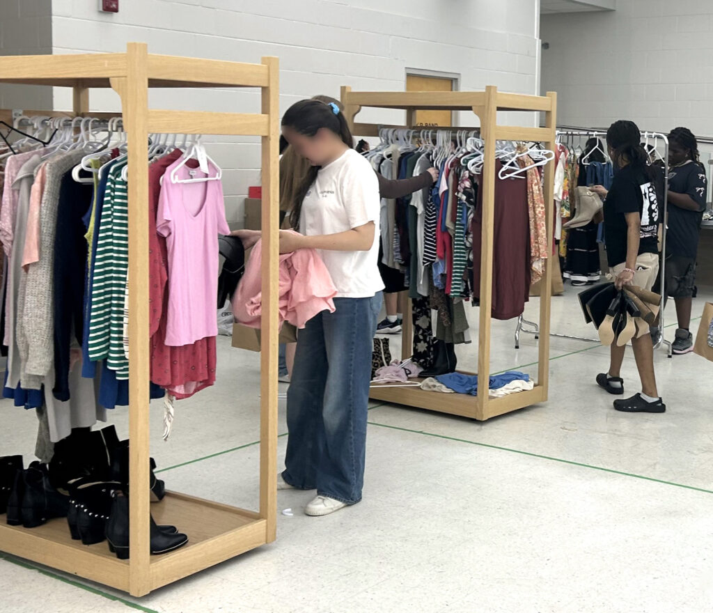 clothing racks with different t-shirts, sweaters, jeans, and longsleeves with young females choosing items