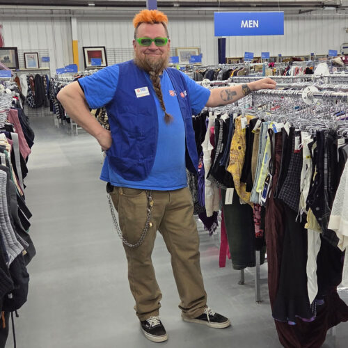 Employee Jeff standing in a Thrift Store aisle with clothing on racks