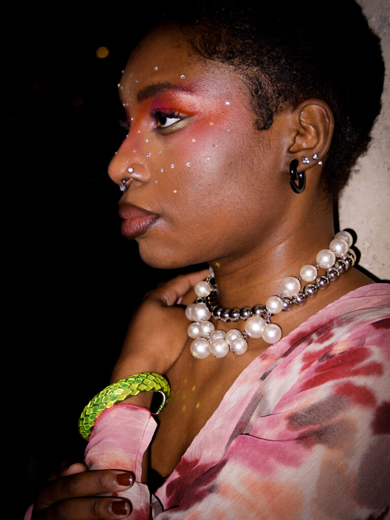 Our collaborator Kendra wearing a pink flowy blouse, pearl necklace and green bracelet